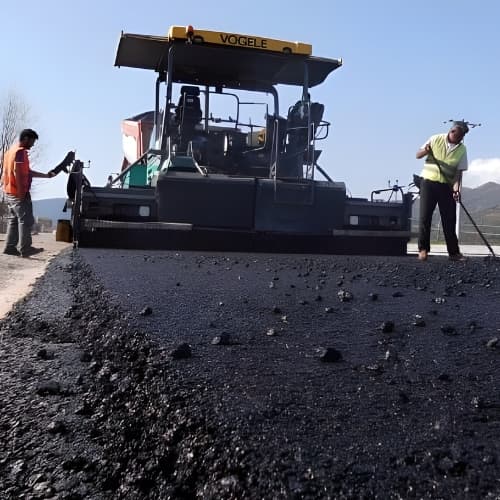 Workers applying cold bitumen or Tiponcoat product on a road with equipment in background